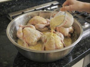 Soaking the chicken in a mixture of lemon, salt, and ginger in a stainless steel bowl.