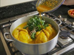 Marinated chicken in a pot over the heat, with a hand pouring the remaining marinade over the chicken