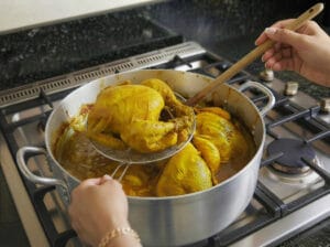 Removing the chicken after it is cooked using a metal strainer and leaving the broth in the pot