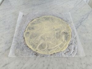 Very thinly rolled dough on baking paper placed on the kitchen countertop