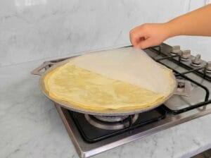 Placing the rolled dough with the baking paper onto a large baking griddle over the stovetop