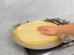 Adding another sheet of rolled dough on top of the first sheet on the baking griddle