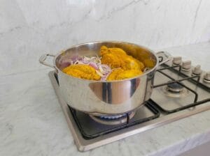 Placing the marinated chicken and sliced onions into a large cooking pot