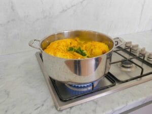 Adding water and a bunch of parsley to the chicken, then bringing it to a boil in a large pot