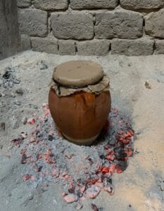 Traditional clay Tangia pot slow-cooking in ashes with glowing embers