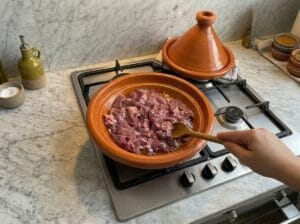 Adding beef liver cubes to the sautéed chopped onions in a clay tagine