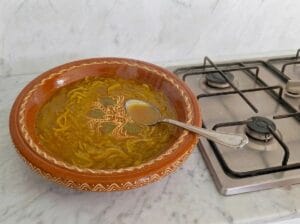 Pouring a portion of the broth into a traditional Moroccan mixing bowl (gasaa) on the kitchen countertop
