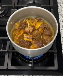 "A pressure cooker containing Tangia meat with whole garlic cloves and a rich, thick, and flavorful sauce