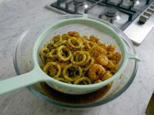 A glass bowl with a colander containing sautéed shrimp and calamari