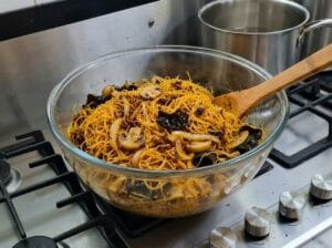 "A glass bowl filled with a mixture of vermicelli noodles, Moroccan chermoula, sautéed button mushrooms, and black fungus