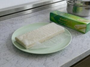 A light green plate holding a sheet of phyllo dough, with the phyllo pastry box placed next to it