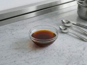 "A glass bowl containing a vibrant orange-red mixture of oil and paprika, specifically prepared for brushing onto Moroccan warqa pastry for pastilla