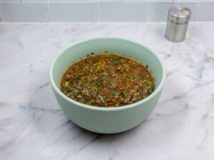 A bowl of Chermoula marinade in a light green bowl on a kitchen marble countertop
