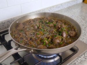 A stainless steel pan with chicken liver, onions, and spices