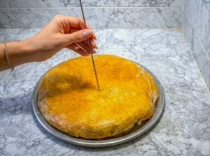 A baking tray with Moroccan fish bastilla, with a hand piercing the pastry using a skewer.