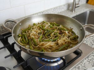 A stainless steel pan with onions and wilted, golden green peppers