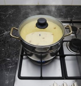 Couscous steaming in a traditional couscoussier pot over the stove