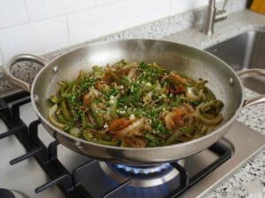 A stainless steel pan with onions, wilted and golden green peppers, and spices