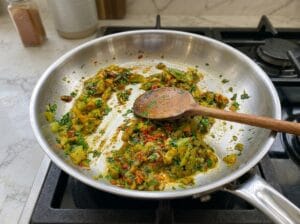 A pan featuring sautéed chopped green bell peppers seasoned with aromatic spices