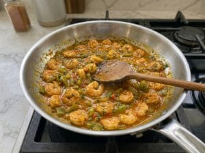 A pan featuring sautéed shrimp with chopped green bell peppers and aromatic spices
