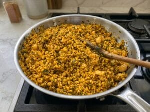 "A pan featuring a flavorful mixture of seasoned grains, such as bulgur or wheat, with small pieces of seafood and fresh herbs