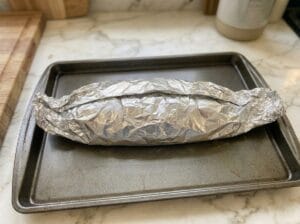 A baking tray with a stuffed fish wrapped in parchment paper and aluminum foil