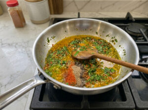 A pan with oil, aromatic spices, and chopped parsley