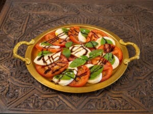 Buffalo mozzarella slices with tomato slices topped with basil leaves and balsamic vinegar.