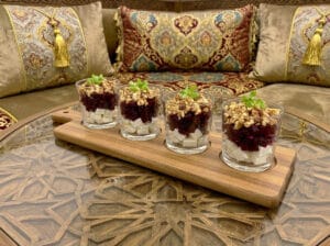 Glasses of beetroot cubes with cheese cubes sprinkled with crushed walnuts presented on a special serving wooden board on an engraved wooden table