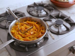 Mashed carrots using a potato masher in a pan
