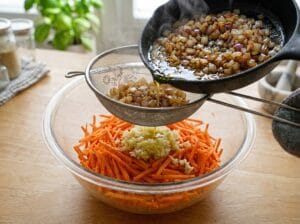 Fried onions poured through a sieve onto grated carrots and garlic