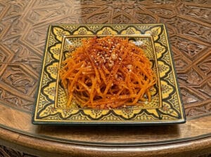 Julienne carrot salad with garlic and chili in a patterned yellow Moroccan plate placed on a wooden table.