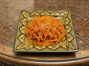 Julienne carrot salad with garlic in a patterned yellow square plate placed on a carved wooden table.
