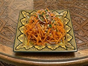 Julienne carrots with red onion in a patterned Moroccan square plate placed on the table.