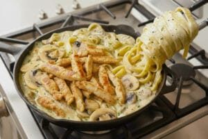 A pan with fettuccine pasta with creamy mushroom sauce and golden-brown chicken strips