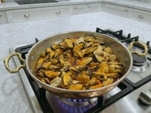 "A traditional copper serving pan filled with mussels cooked in a flavorful Moroccan chermoula sauce
