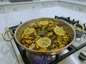 "A traditional copper serving pan filled with mussels cooked in a flavorful Moroccan chermoula sauce
