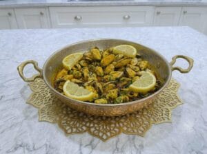 "A traditional copper serving pan filled with mussels cooked in a flavorful Moroccan chermoula sauce