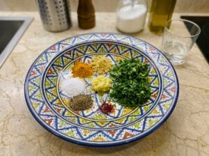 Moroccan decorative plate filled with meat marinade spices, chopped herbs, minced garlic, and a glass of water