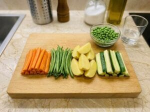 Potato, carrot, green bean, and green zucchini (zucchini) batons, cut into uniform sticks of the same size, along with peas, in a glass bowl.