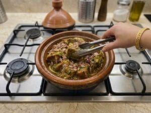 Meat in the tagine with spices, a hand holding tongs and turning the meat and onions