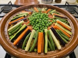 Vegetables in the tagine arranged in sticks, with green peas in the center of the vegetables