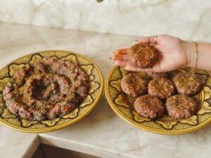 Plate with kofta mixed with spices, a plate with kofta patties, and a hand making kofta patties