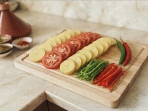 Chopped vegetables potato slices, tomato slices, and green and red pepper fingers on a wooden board