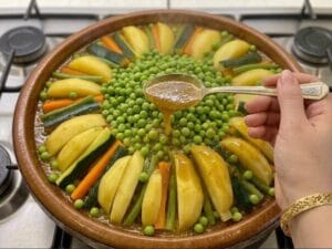 A hand holding a spoon and ladling broth over the vegetables