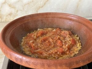 Tagine with oil, finely chopped golden-brown onion, and well-cooked, melted tomatoes