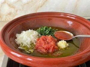 Red earthenware tagine with a tomato, finely grated onion, parsley, finely chopped garlic, and a spoon of light tomato sauce
