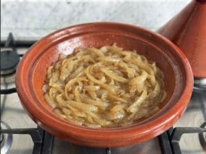 Red earthenware tajine containing golden-brown onions with oil