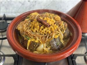 Conger eel fish with marinade, onions, raisins, and a cinnamon stick in a Moroccan tajine over the fire